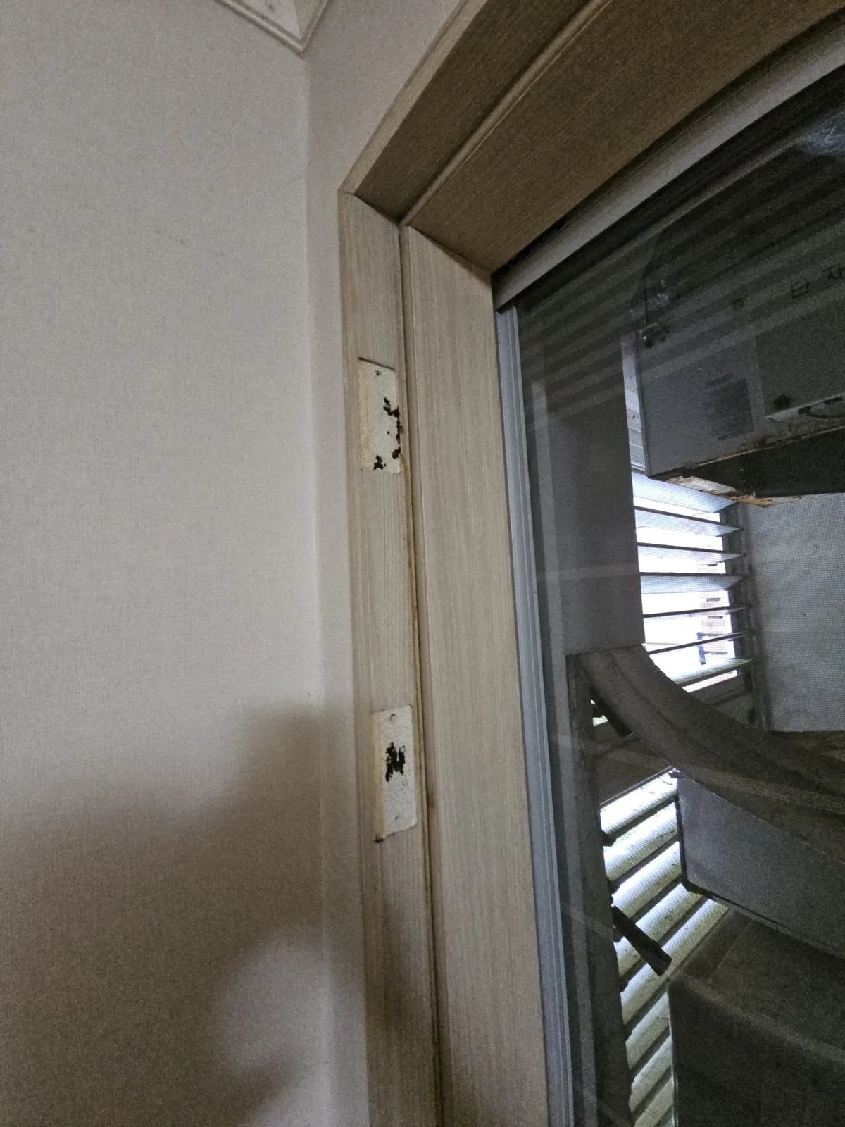 문틀 세로대 면에 사각형 경첩 받침판 두 개가 나사로 고정돼 있고 표면에 검은 오염 자국이 남아 있다.