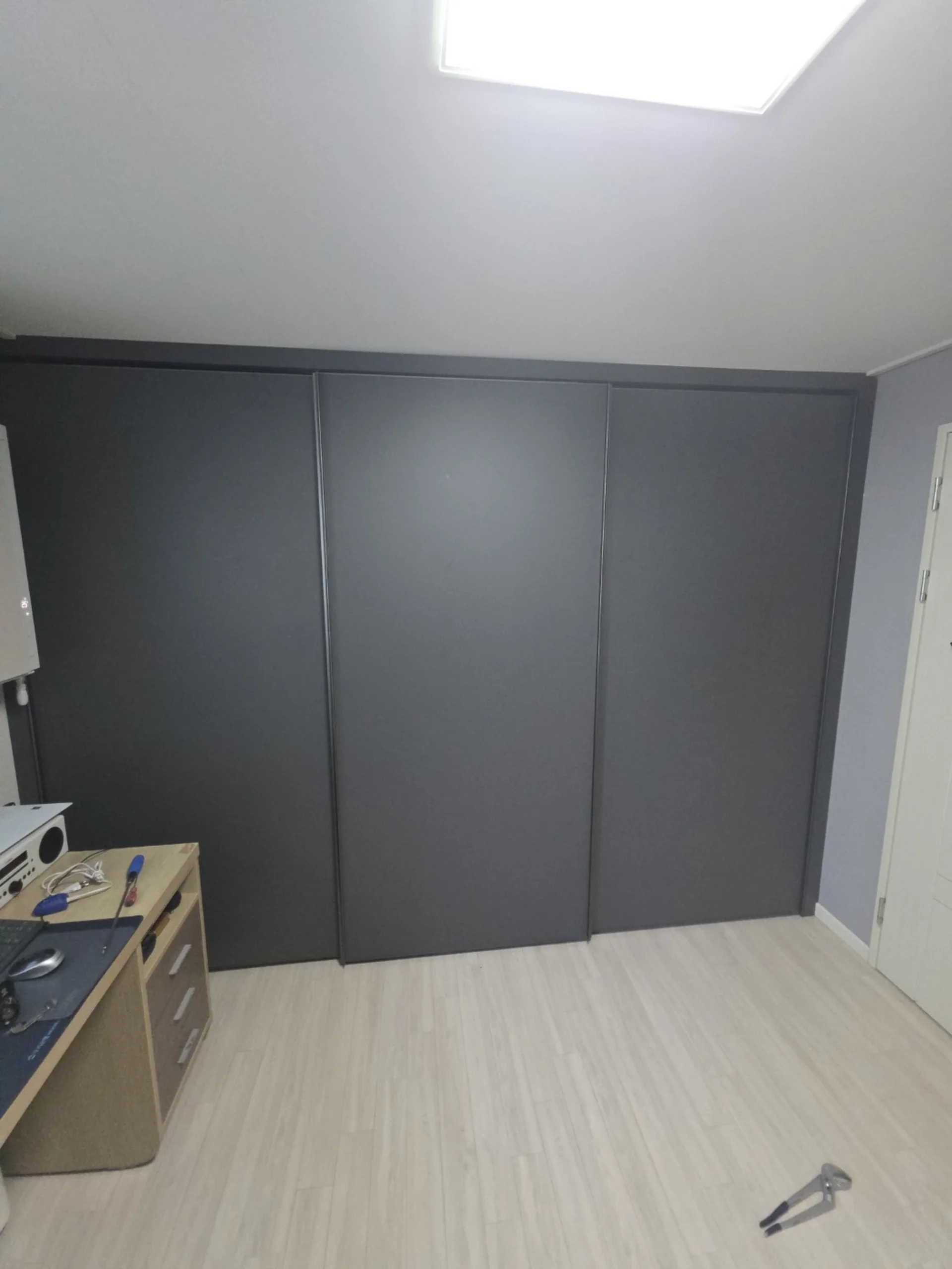 방 한쪽 벽면 전체를 차지하는 붙박이장 슬라이딩 도어 세 짝이 짙은 회색으로 마감되어 있다.